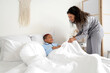 © Pixel-Shot - Young African-American woman covering her little son with blanket in bedroom