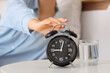 © Pixel-Shot - Woman turning off alarm clock on bedside table with glass of water in bedroom, closeup