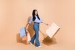 © deagreez - Stylish young woman in casual attire holding shopping bags with a joyful expression, posing against a neutral background