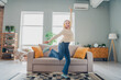 © deagreez - Young woman joyfully dancing in a cozy living room with modern interior design and natural daylight streaming through the windows