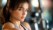 © PFU - A captivating young woman with striking brown eyes and a confident gaze, her dark hair styled elegantly, captured in soft, warm lighting against a blurred gym backdrop.