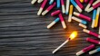 © Akstem - Colorful matches scattered on a wood surface, one lit, creating warmth and light.