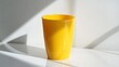 © ULFAITA - Bright yellow plastic tumbler on a white surface.