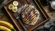 © พงษ์ศักดิ์ อ่อนพฤกษ์ - A beautifully plated banana roti, topped with chocolate drizzle, placed on a rustic wooden tray with a fork, fresh banana slices, and a dusting of powdered sugar.