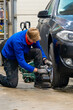 © Aimur - A car service worker changes winter tires to summer wheels on a black automobile. Automotive technician in protective gloves using an impact driver for seasonal tire replacement