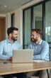 © Viktor - Two businessmen partners at work in office talking, smiling at laptop, discussing new investment project. Happy male executives friendly conversation at desk, work together. Teamwork meeting,