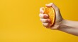 © Postmodern Studio - Hand squeezing fresh orange against bright yellow background with juice dripping