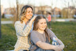 © Dejan - A casual yet heartfelt moment of a mother braiding her daughter’s hair while both enjoy a calm afternoon in the park.