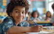 © Darya - Smiling boy with curly hair writing in classroom. Childhood education and joy concept.
