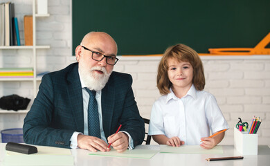 Fototapete - Senior teacher and school child. Mature teacher helps school child learn. School teacher and child in classroom. Teacher in school on lesson teach child. Kids education and learning.