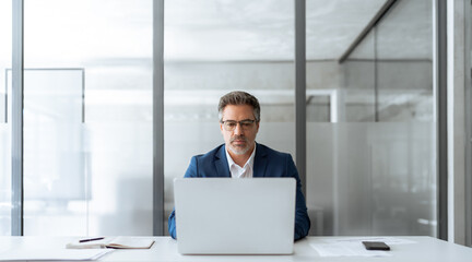 Focused senior businessman entrepreneur sitting at desk working on financial project, looking thinking at screen. Mature 50s Latin business man ceo manager using laptop computer in office. Copy space