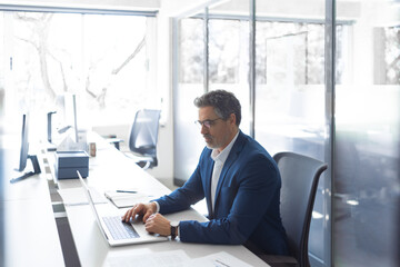 Mature 50s Latin business man ceo manager using laptop computer in office. Focused senior businessman entrepreneur sitting at desk working on financial project, typing looking at screen. Copy space