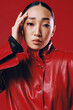 © SHOTPRIME STUDIO - Fashionable asian brunette in a red leather jacket posing with eyes closed against a red background