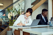 © bnenin - Focused Woman Taking Notes at a Workplace with Laptop and Coworkers