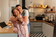 © DusanJelicic - Young couple wearing pajamas is standing in their modern kitchen, embracing each other tenderly with a video call visible on a laptop placed on the counter