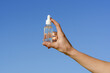 © Daryna  - Female hand holding a transparent glass jar of serum with a pipette on a blue sky background. Concept of aesthetics and beauty care products, smoothing wrinkles and moisturizing the face.