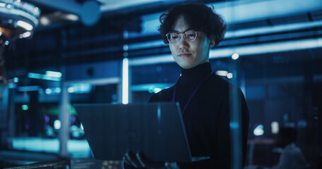 asian software developer using a laptop to monitor the work of a quantum computer, focusing on data 