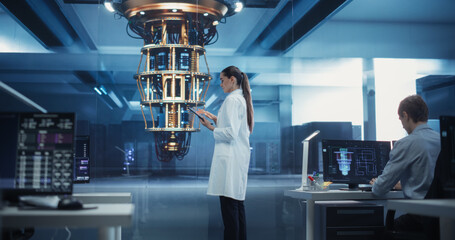 Female Scientist Working on Quantum Computer Hardware, Using Tablet Computer to Access Technical Specifications and Control Processor Parameters. Group of Developers Work on AI Behind Their Desks