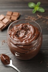 Wall Mural - Delicious chocolate pudding in glass and spoon on wooden table, closeup
