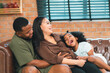 © chokniti - Heartwarming family moment as an African American father and daughter share playful time together on the couch, surrounded by love, laughter, and the warmth of home, while mom gently looks on with joy