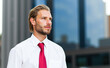 © Minerva Studio - Young businessman looking away with office buildings in background