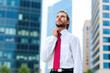 © Minerva Studio - Businessman adjusting his tie looking up at skyscrapers in business district