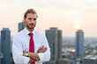 © Minerva Studio - Businessman posing with arms crossed on rooftop at sunset with cityscape in background