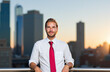 © Minerva Studio - Businessman posing on rooftop at sunset with city skyline in background