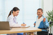 © Ekkasit A Siam - Asian senior woman sitting in wheelchair lifting cardigan during medical consultation with female doctor writing on clipboard, showing health checkup interaction and elderly patient care in hospital.