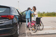 © Martí Rosselló - Assistant helping young woman with cerebral palsy into car - Caregiver supports female patient in transferring from wheelchair to parked vehicle. Concept of cerebral palsy.