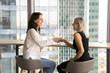 © fizkes - Making deal. Two diverse age businesswomen handshake on meeting at office table enjoy successful partnership reaching agreement. Aged hr manager greet happy young female applicant with receiving job