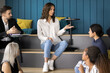 © fizkes - Discussing idea. Young woman university student employee speak to multinational diverse classmates coworkers group lead discussion share plan opinion with mates at multilevel classroom conference room