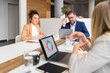 © Moon Safari - Businesswoman reviewing report on her laptop while discussing business performance with coworkers in meeting