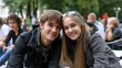 © Mykhailo - Young happy couple smiling at outdoor event with blurred background of people and trees in park