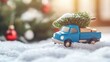 © tashechka - A small blue toy truck carries a Christmas tree, traveling across snowy ground with holiday decorations in the background