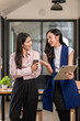 © Wasana - Two women are standing in front of a desk, one of them holding a cup of coffee