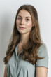© Wilker - Serene Portrait of a Young Woman in Her Early Twenties, with Long Brown Hair and a Sage Green Blouse, Exuding Calmness and Professionalism against a Clean White Background.