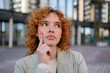 © Westend61 - Redhead woman in blazer thinking outdoors in urban setting