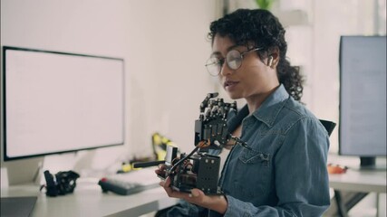 Asian female engineer demonstrates robotic arm while communicating through earbud in a modern tech lab. Concept of innovation, robotics, and women in STEM.