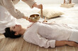 © New Africa - Woman undergoing singing bowl therapy lying on floor indoors