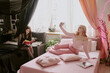 © AnnaStills - Two sisters spending time in room, goth teen sitting carefully on edge of bed and reading book while her exact opposite blond sister dressed in pink taking selfie