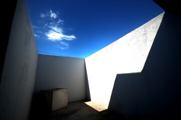 Poster - Bright sunlight filters into an empty courtyard surrounded by white walls under a clear blue sky