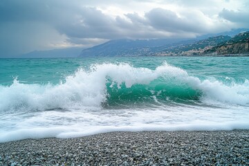 Aufkleber - Ocean wave crashing on pebbled beach with stormy sky over distant mountains in late afternoon
