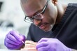 © Georgy - A laboratory worker, who is African American and wears latex gloves, uses a probe and mouth mirror to check the condition of artificial teeth in a modern lab
