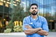 © Liubomir - A healthcare professional stands outside, arms crossed, and is wearing scrubs and a stethoscope around his neck. The medical worker appears confident.