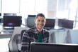 © wavebreak3 - Young man working on desktop computer in modern office, smiling at camera with computer monitor
