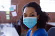 © wavebreak3 - Diverse woman sitting at clinic desk, wearing blue scrubs and mask with sticky notes, copy space