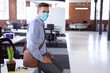 © wavebreak3 - Young man sitting on desk edge in industrial open-plan office, wearing face mask and carrying bag