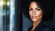 © Biggy - Confident woman with dark curly hair, intense gaze, wearing a black blazer