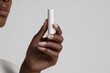© emzee - Woman's Hand Holding White Cylindrical Tube Against Gray Background